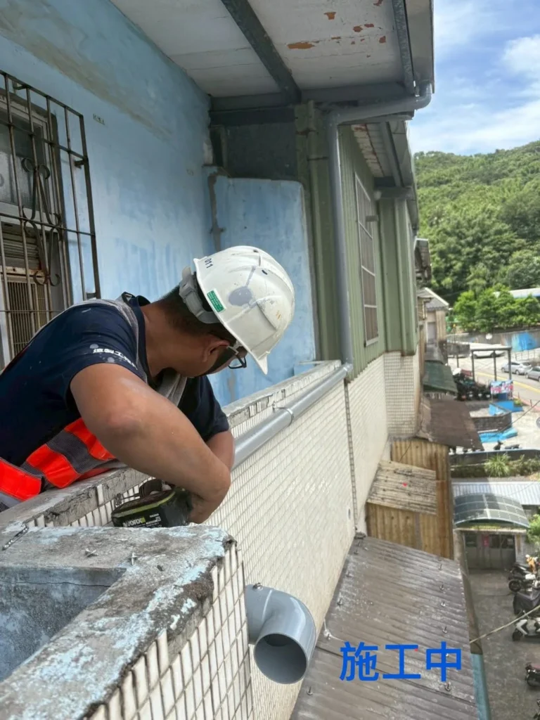 中平街洩水管施工中,施工人員將管件沿外牆位置調整固定